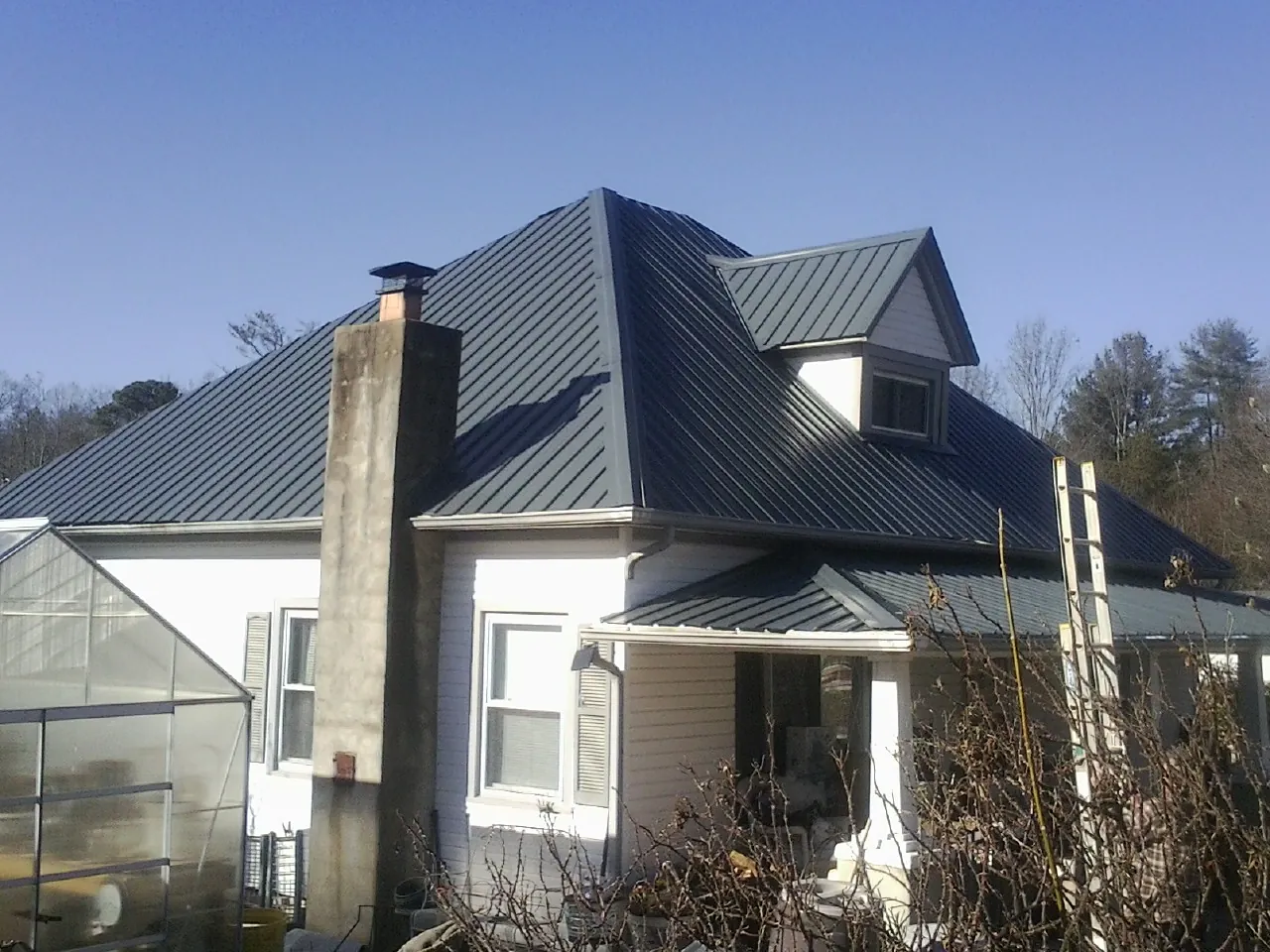 Dark blue standing seam metal roof on a white farmhouse with dormer — Slate & Tile Roof Repair by Roofing Brothers in Morton Grove