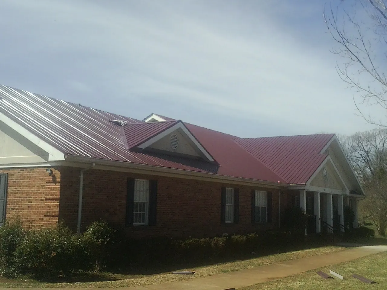 Red metal roof with gabled entries on a long brick building, from a Hail Damage Roof Repair job in Morton Grove