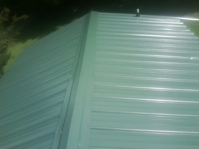 New green metal panels meeting at the ridge of a roof — Flat Roof Repair work by our crew in Morton Grove