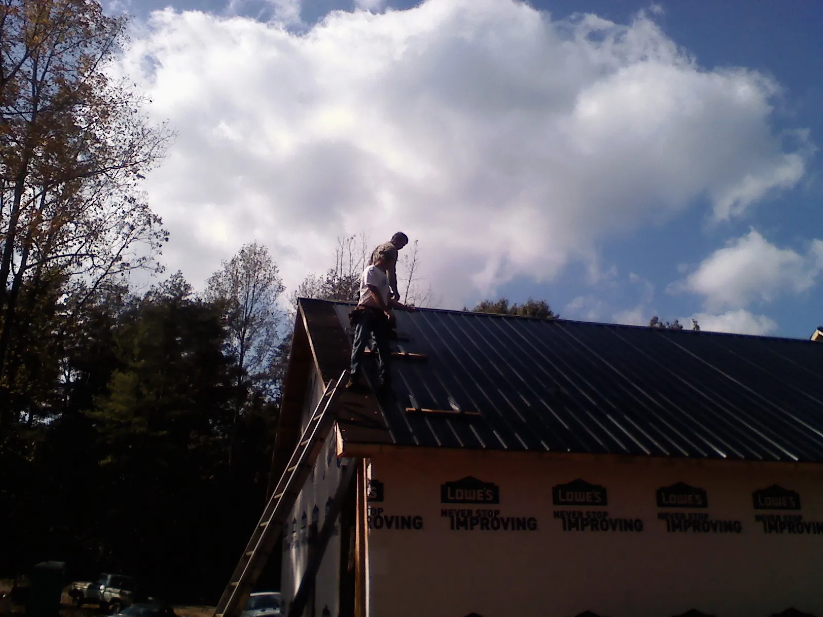 Roofer fastening dark metal panels high against a cloudy sky, from a Roof Inspection job in Morton Grove