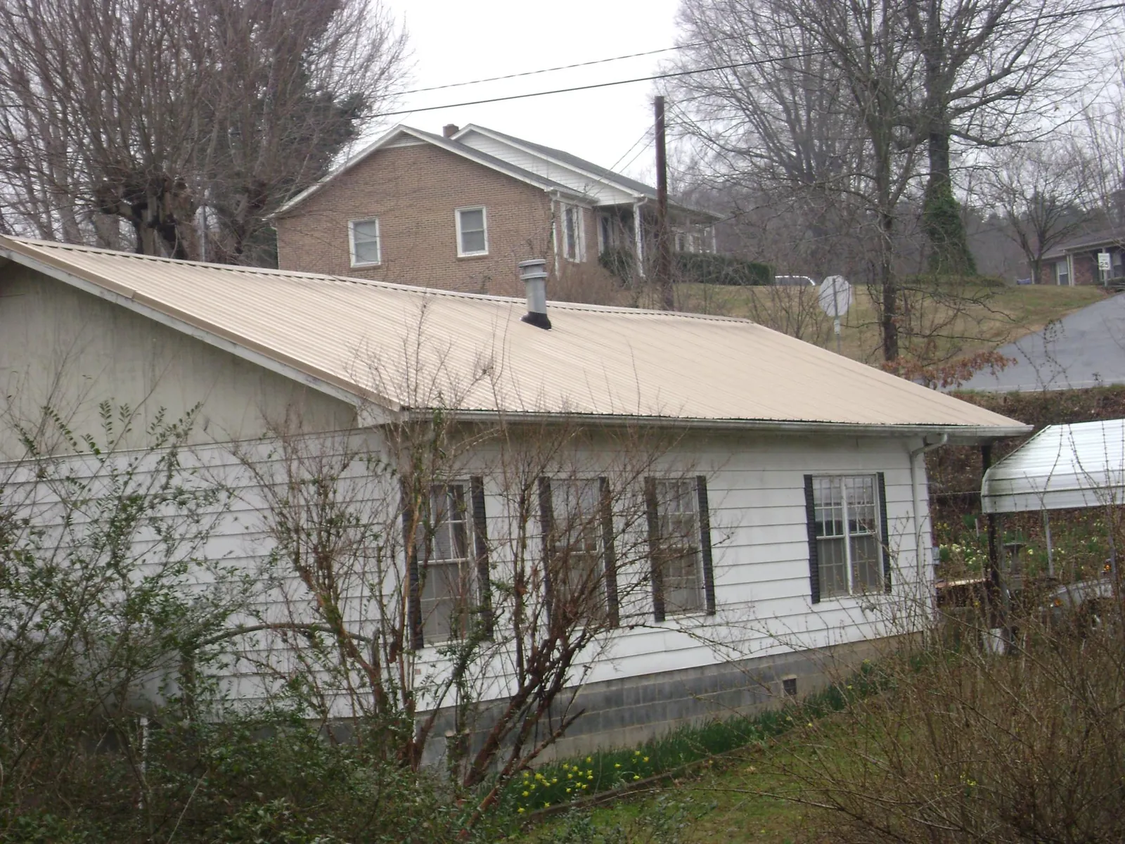 Tan metal roof on a white sided house set into a hillside — Commercial Roofing by Roofing Brothers in Morton Grove